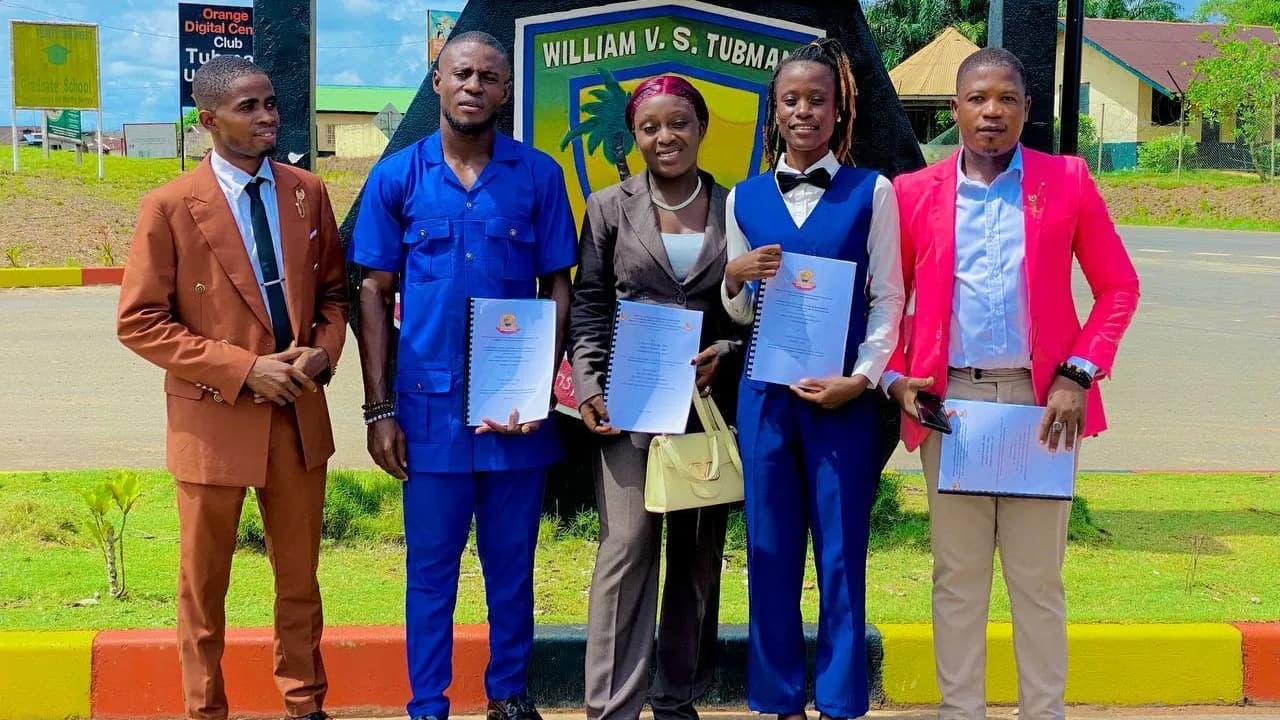 Five students of the College of Engineering and Technology, smartly dressed and holding bound reports, in front of the William V.S. Tubman University sign